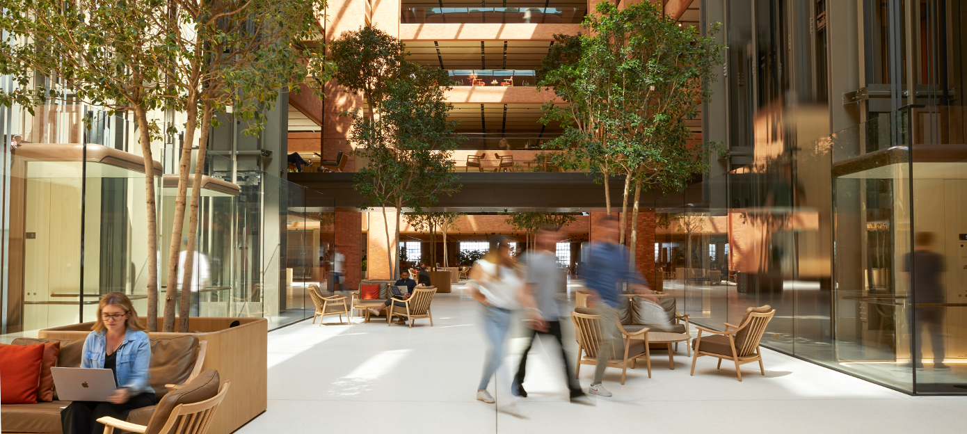 Apple ekip üyelerinin toplantı yaparken, yürüyüp geçerken ve farklı oturma düzenlerinde çalışırken göründüğü Battersea avlusunun güneş ışığı alan alt katı.