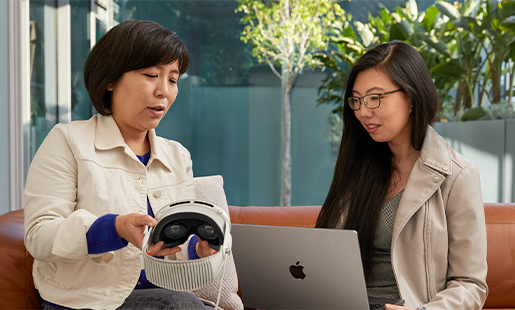 Kapısı avluya açılan bir alanda MacBook kullanan Jessica, ona Apple Vision Pro’yu gösteren bir Apple çalışanıyla oturuyor.