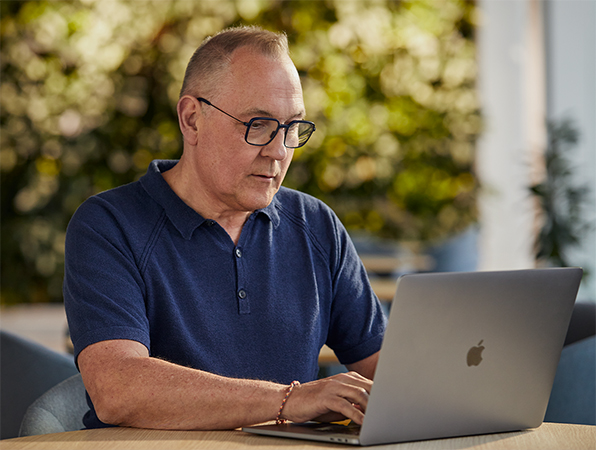 Apple Yazılım ve Hizmetler çalışanı dışarıda bir MacBook’ta çalışıyor ve arka planda bitkiler görünüyor.